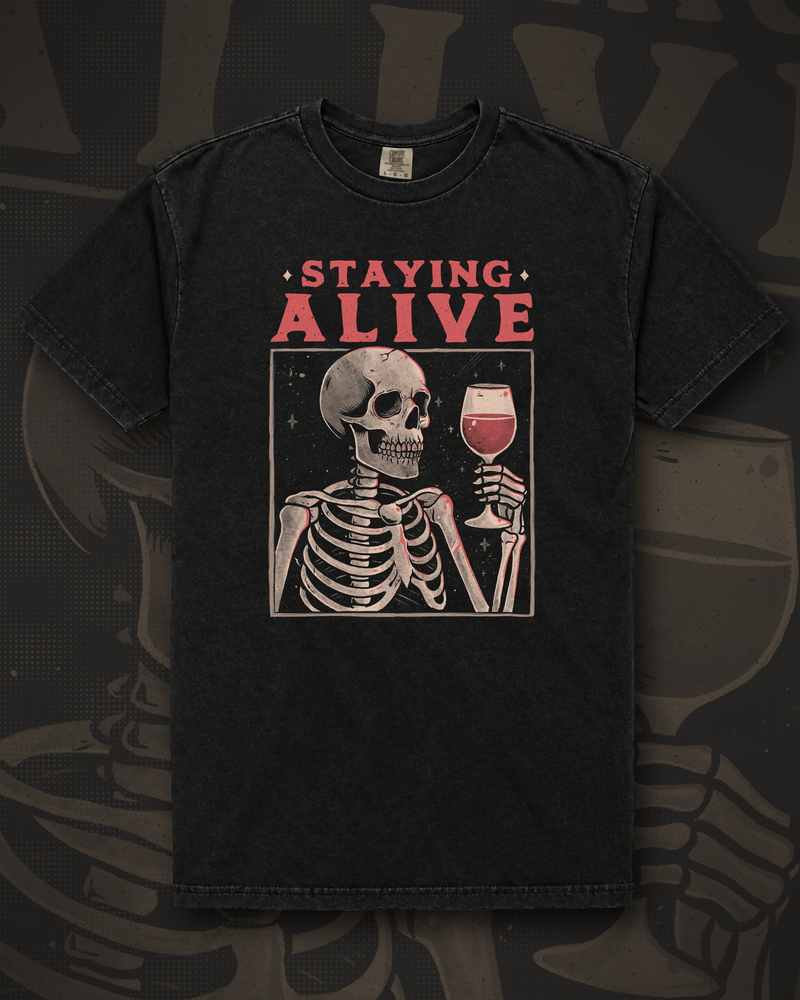 Skeleton raising a glass of red wine inside a rectangular frame under the words Staying Alive graphic on black t-shirt – Staying Alive With Wine Tee by CREEPTEE