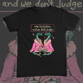 Two snakes in pink fur-trimmed robes holding martini glasses beneath a speech bubble reading We Lisssssten And We Don't Judge graphic on black t-shirt – We Listen And We Don't Judge Tee by CREEPTEE